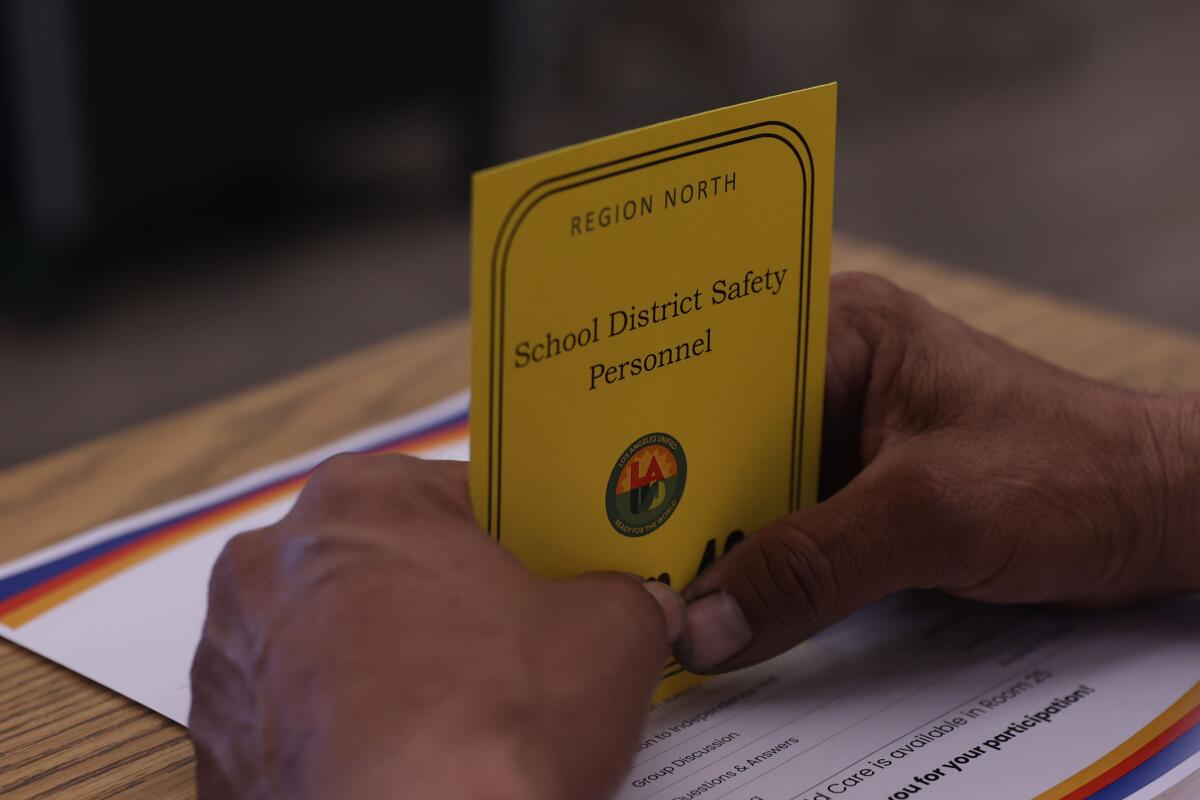 A man's hands hold a card reading "School District Safety Personnel." 