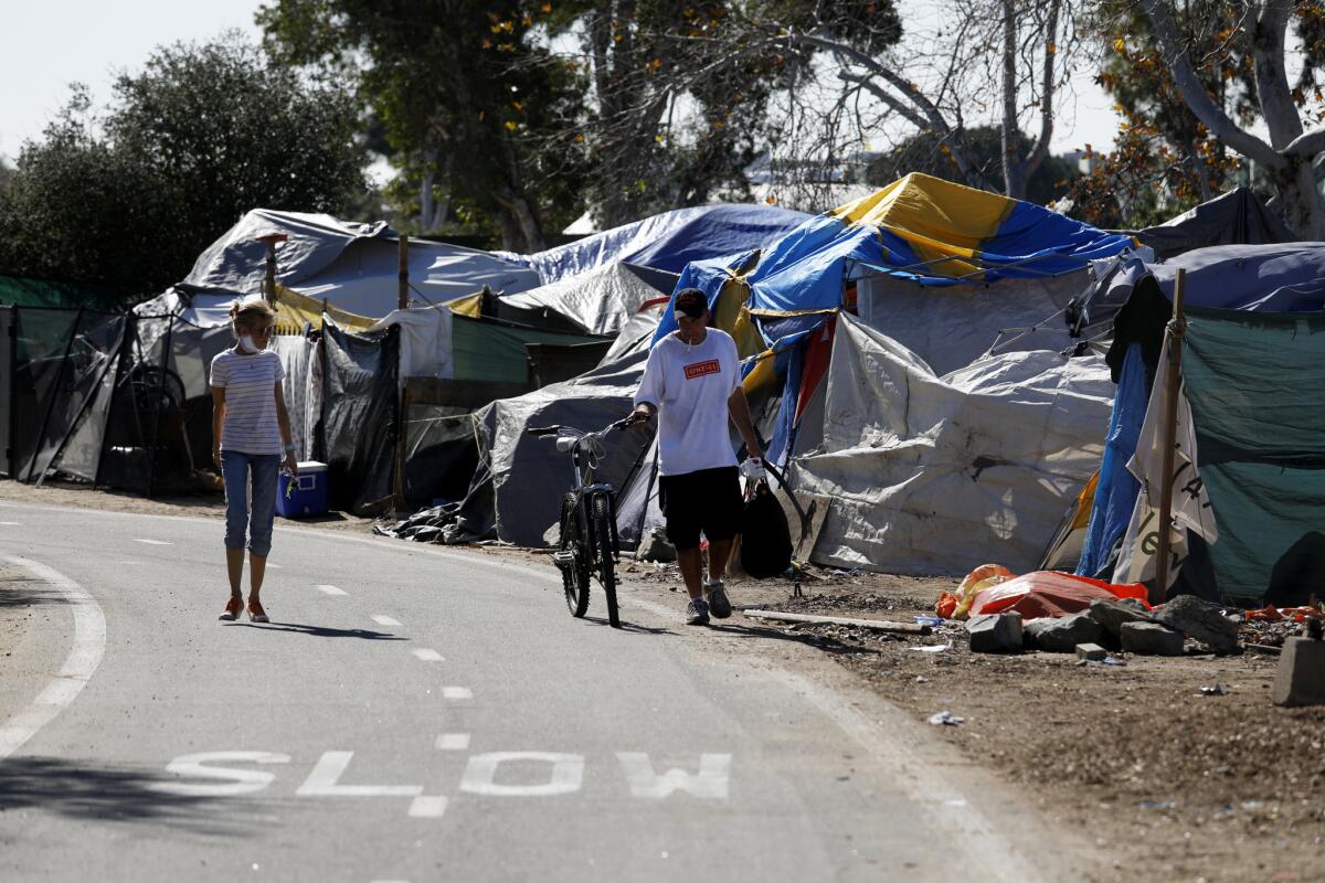 In this 2018 file photo, a homeless man and woman walk along an encampment at the Santa Ana river trail in Orange County. County officials have entered into an agreement with a hotel operator to house and treat unsheltered people amid the coronavirus.