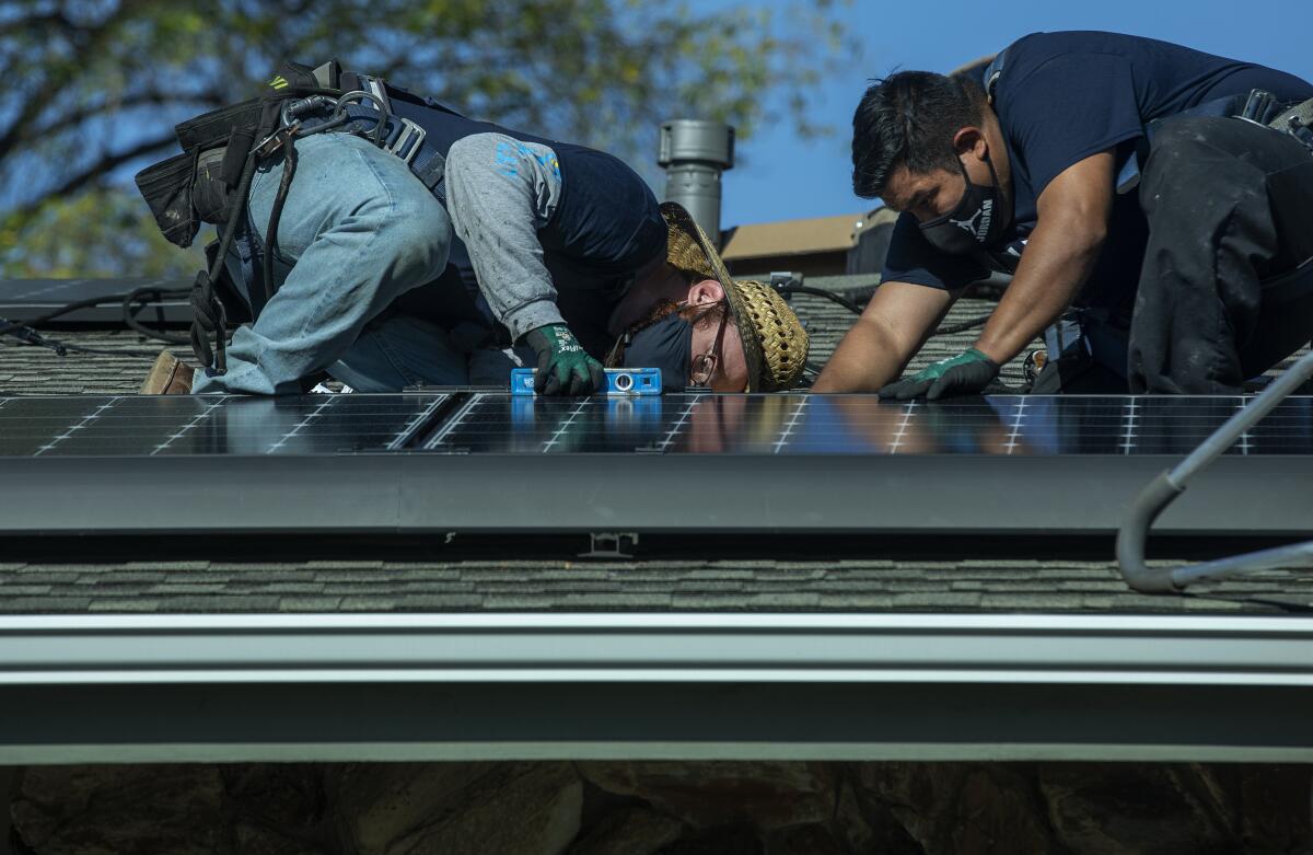 A man uses a level as he and another man install a rooftop solar panel.