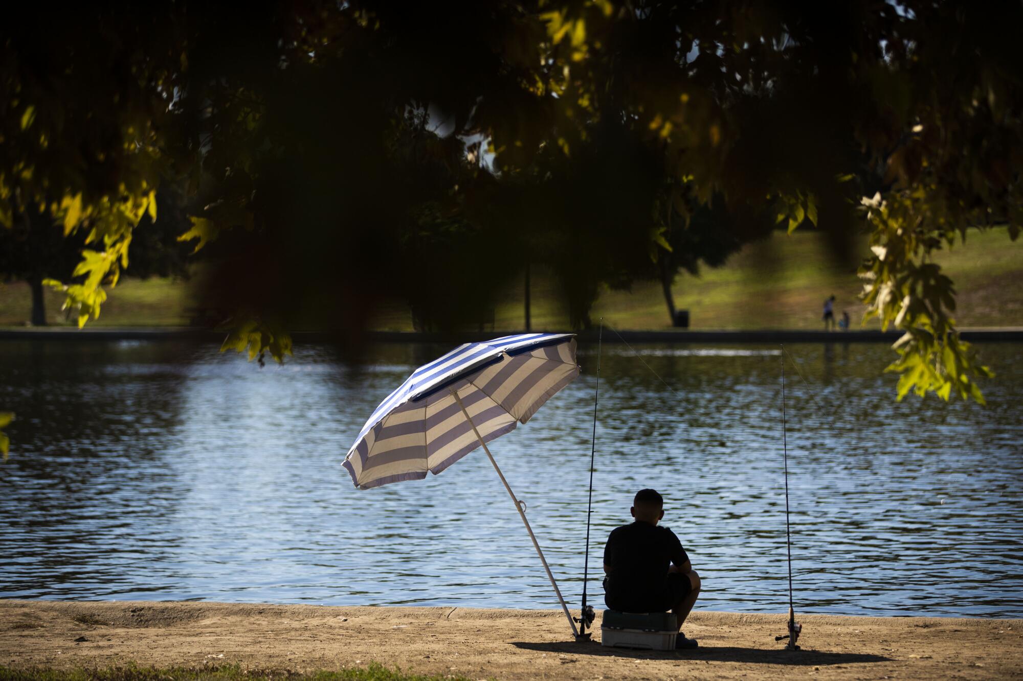 A boy, in the shade of an umbrella, fishes at Lake Balboa on a hot day. 