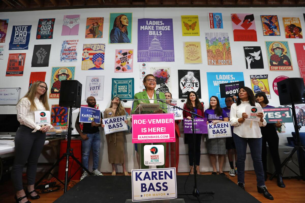 Karen Bass speaks at podium with campaign signs, including one that says "Roe-vember is here!"