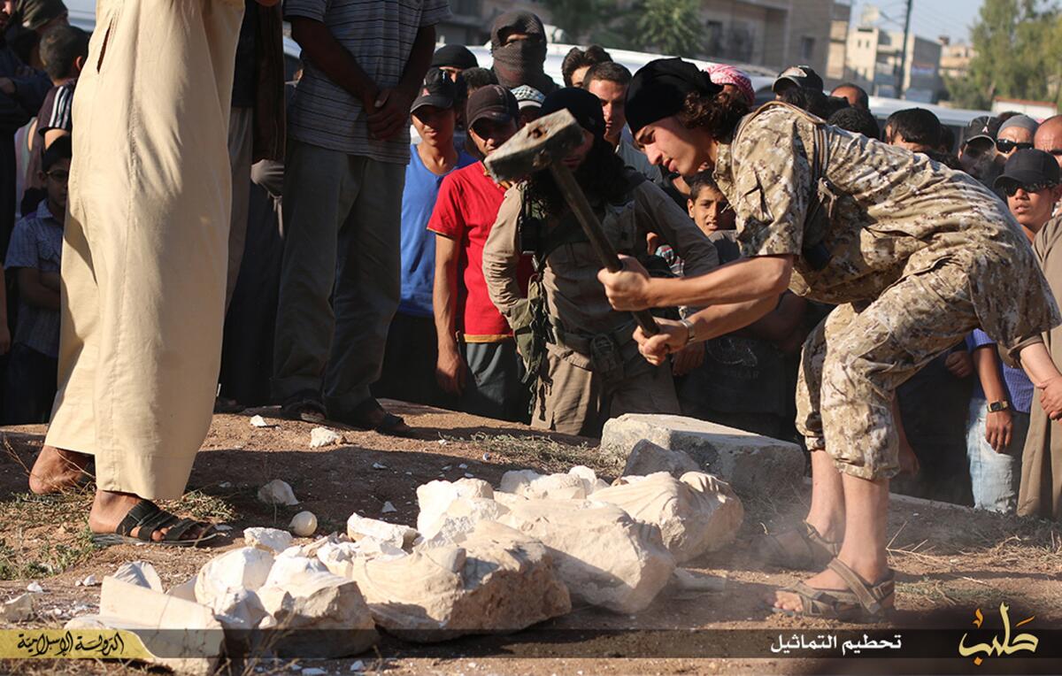 In this image posted on a militant website by the Aleppo branch of the Islamic State group on Friday, July 3, 2015, which has been verified and is consistent with other AP reporting, a militant smashes items that the group claims are smuggled archaeological pieces from the historic central town of Palmyra, Syria. An IS statement says the busts were found when the smuggler was stopped at a checkpoint and was later referred to an Islamic which ordered that they be destroyed and the man be whipped. (militant website via AP)