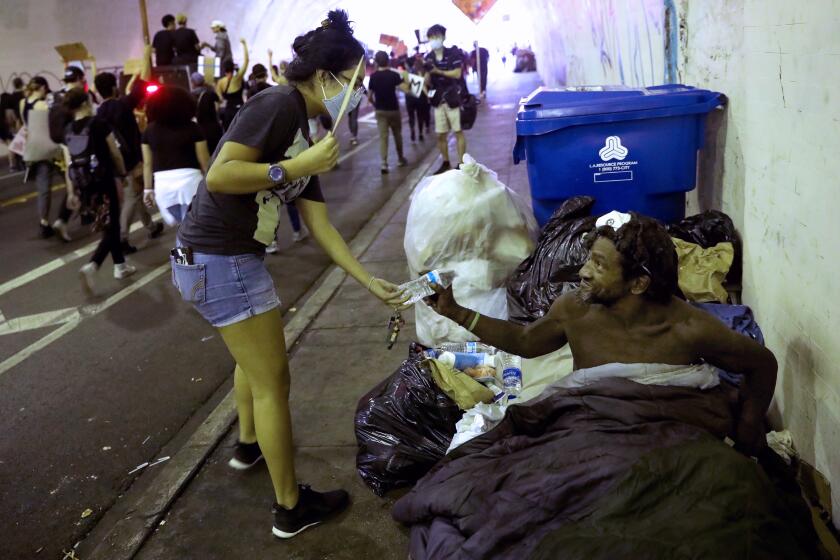 LOS ANGELES, CA - JUNE 04: A protestors hands Isaac D., right, homeless, a bottle of water as he watches protestors march in solidarity against last week's death of George Floyd in Minneapolis, in the 2nd Street Tunnel on Thursday, June 4, 2020 in Los Angeles, CA. Homeless are exempt from the curfew in place for the protesters. (Gary Coronado / Los Angeles Times)