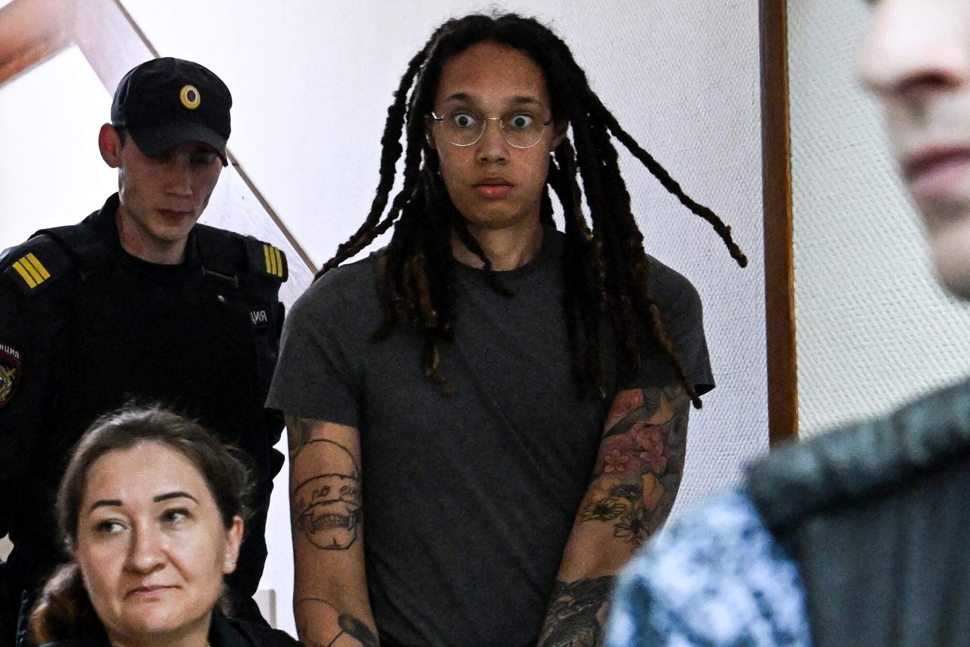 Brittney Griner, wide-eyed, surrounded by uniformed people.