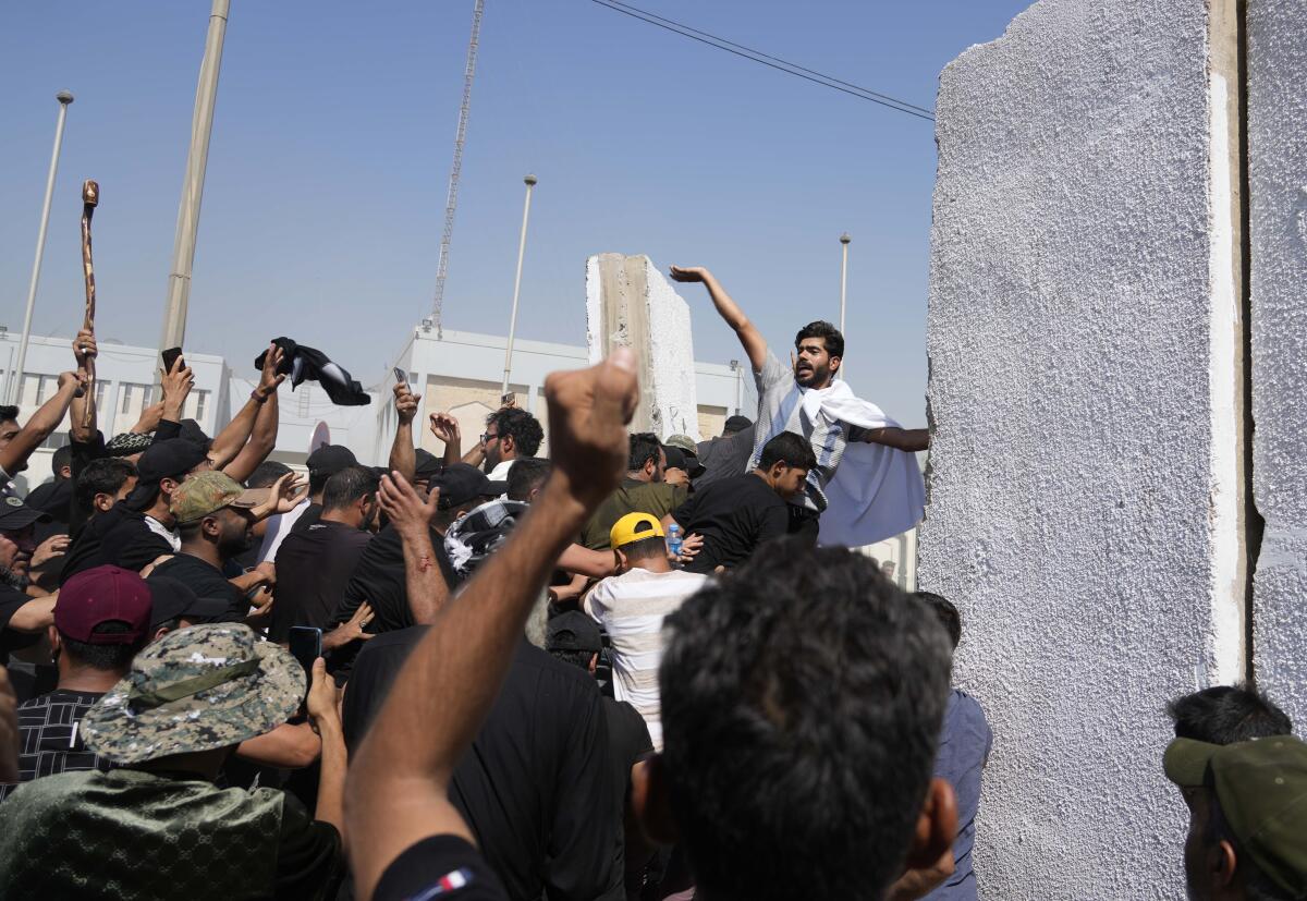 People raise their hands near a dark-haired man with a beard standing near concrete barriers 