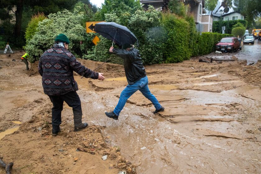 Studio City, CA - January 10: Bud Tate, 60, left, gives a hand to Anthony Ivancich, 80, jumping over flooded street in heavy rain and mudslide at 3700 block of North Fredonia Drive on Tuesday, Jan. 10, 2023 in Studio City, CA. (Irfan Khan / Los Angeles Times)