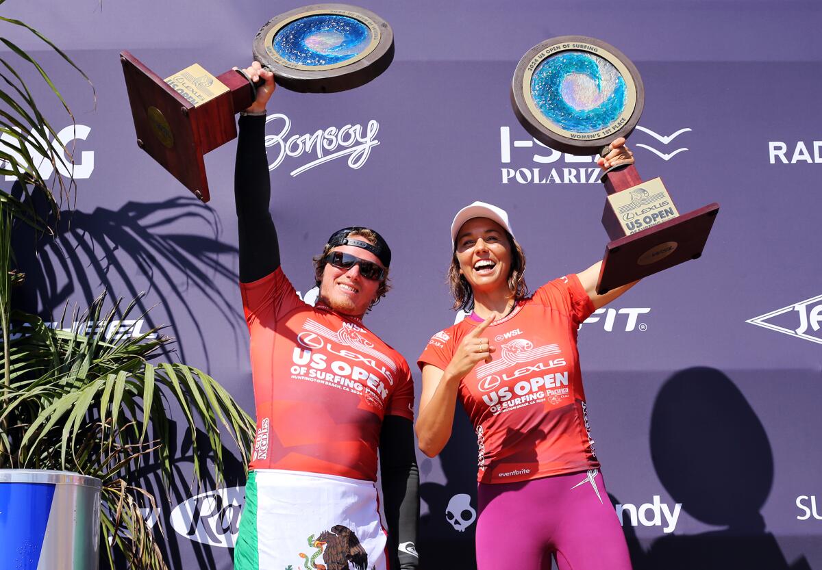 Alan Cleland of Mexico and Sally Fitzgibbons hold up their the 2024 U.S. Open of Surfing trophies.