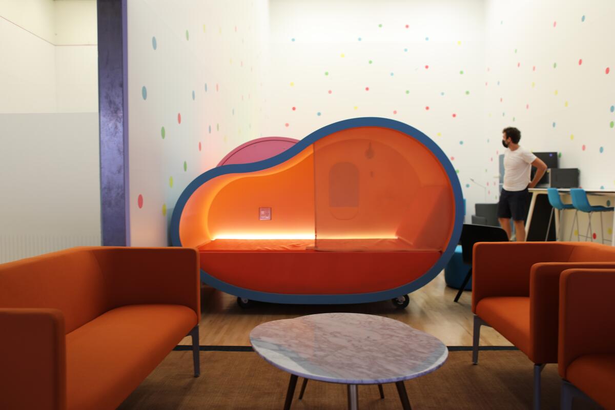 Gus Wendel is seen in the background of a jelly-bean-shaped sleeping pod in a room painted with polka dots.