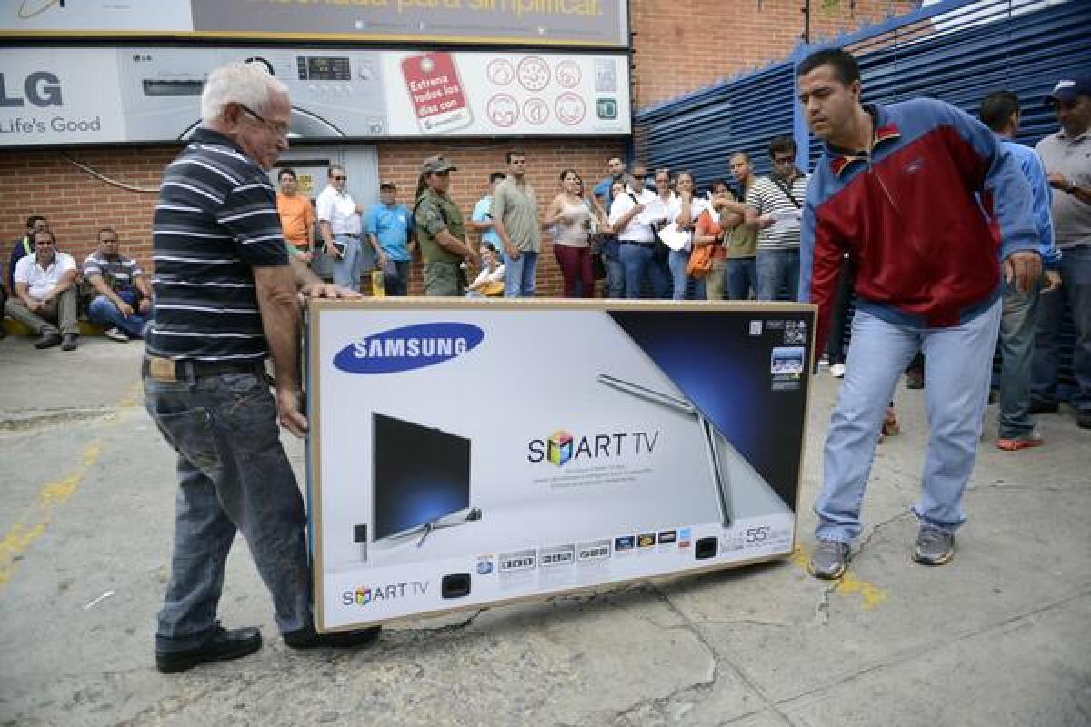 Two men carry a recently purchased TV as many others line up outside a shop in Caracas, Venezuela, after President Nicolas Maduro ordered the "occupation" of a chain of stores accused of illegally raising the prices of their items.