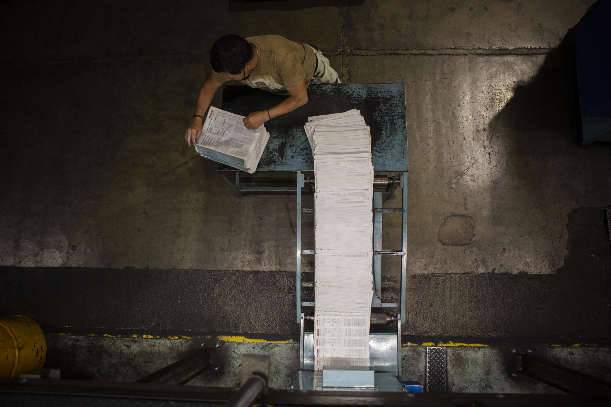 A worker stacks freshly printed newspapers.