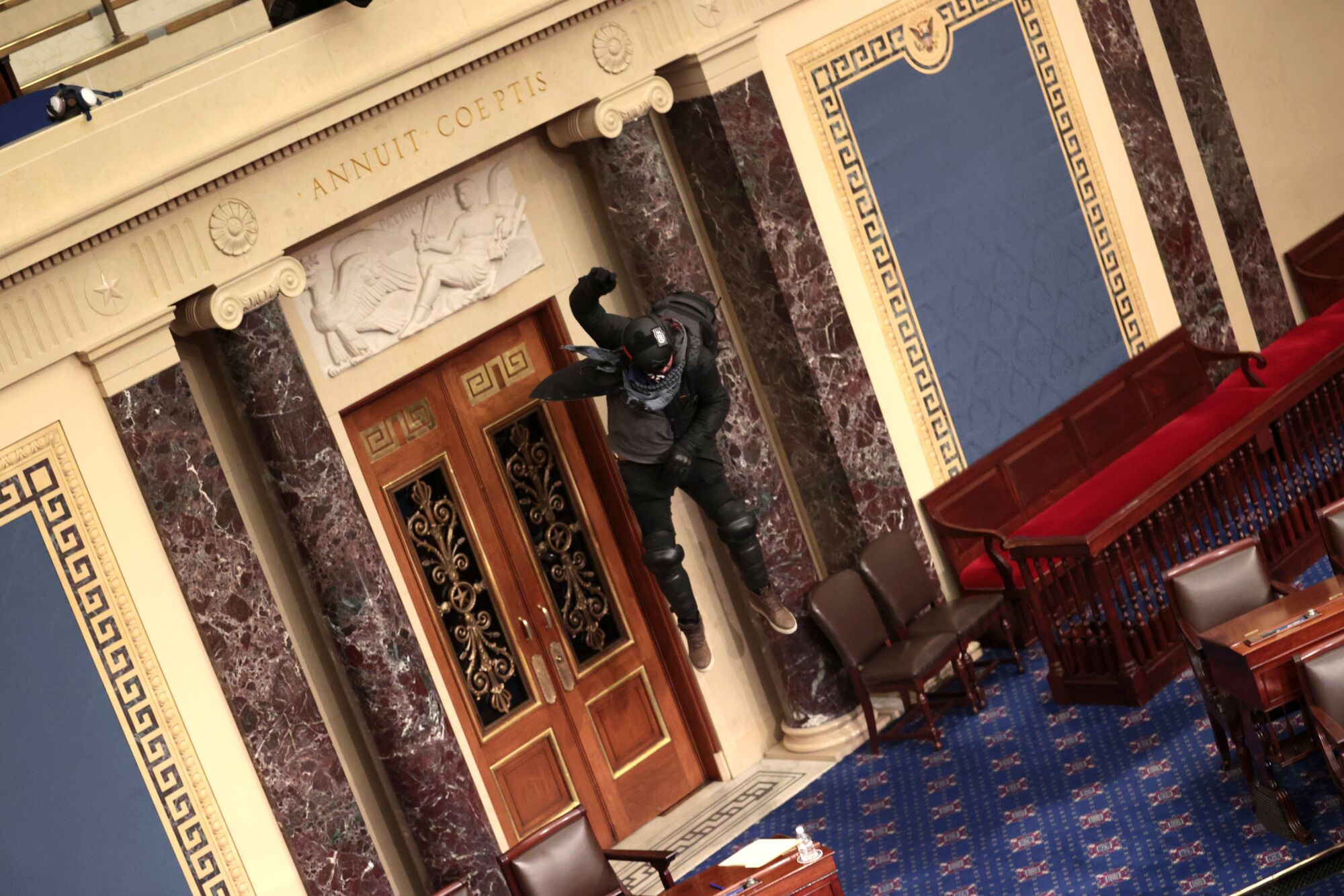 A man is shown dropping from a low balcony inside the Senate chamber.