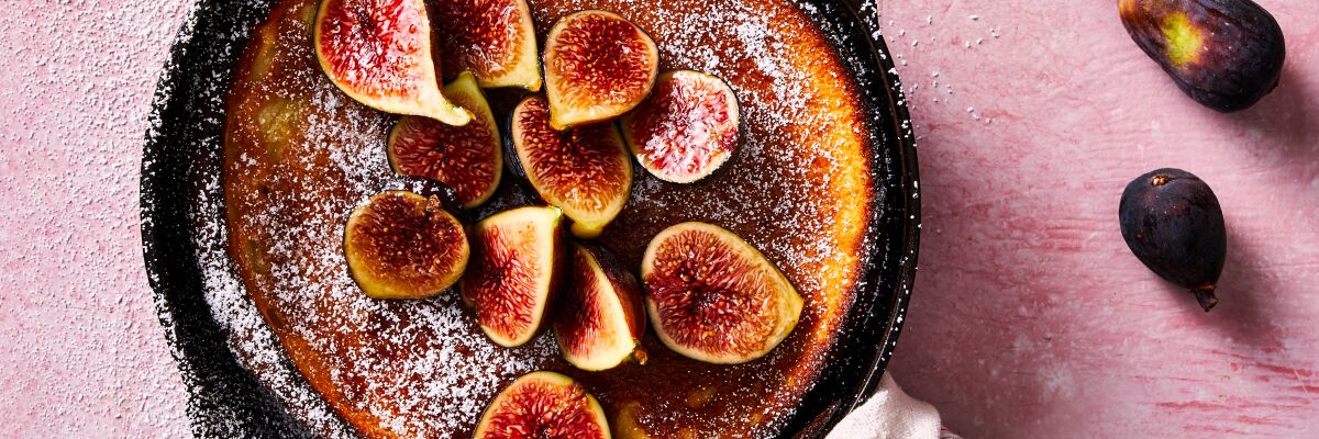 A Dutch baby pancake dusted with powdered sugar and topped with honeyed figs, still in the skillet.