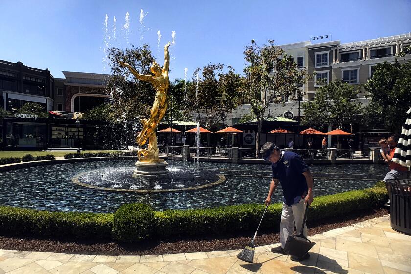 A custodian is seen sweeping before a large fountain bearing a golden sculpture of a soaring nude male figure