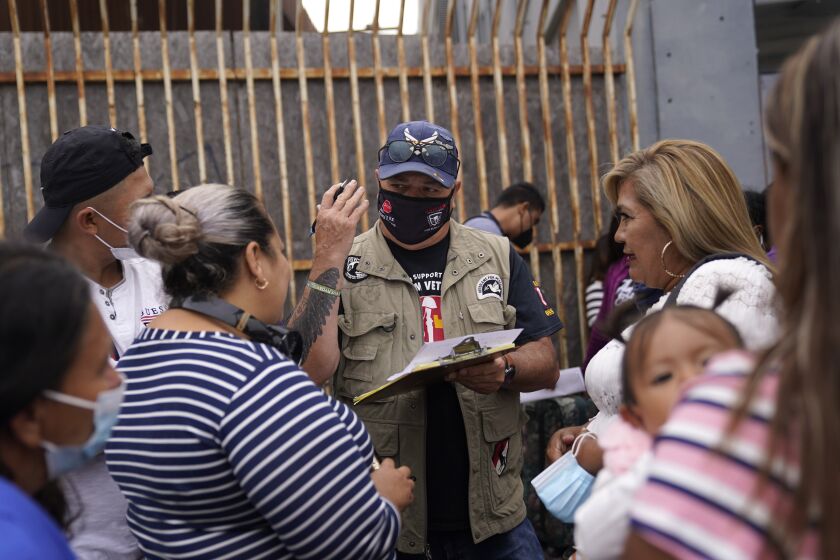 Robert Vivar of the Unified U.S. Deported Veterans Resource Center , center, talks with migrants as they wait to cross into the United States to begin the asylum process Monday, July 5, 2021, in Tijuana, Mexico. Dozens of people are allowed into the U.S. twice a day at a San Diego border crossing, part of a system that the Biden administration cobbled together to start opening back up the asylum system in the U.S. Immigration advocates have been tasked with choosing which migrants can apply for a limited number of slots to claim humanitarian protection. (AP Photo/Gregory Bull)