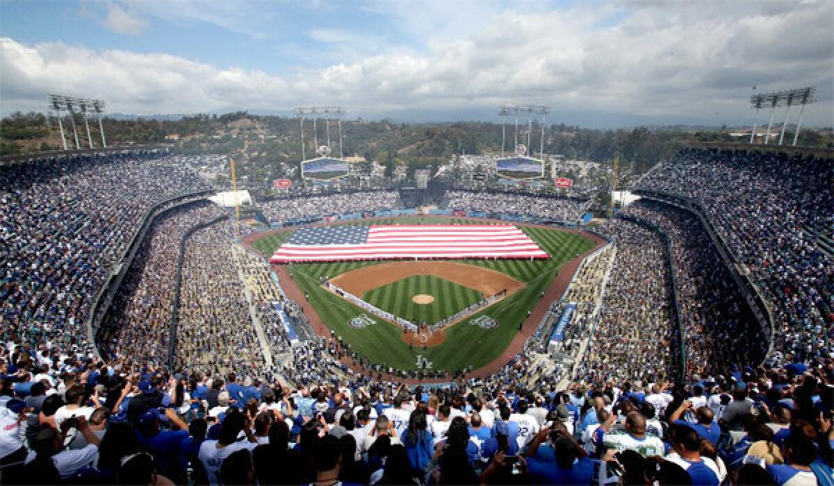 The crowd and participants stand for the national anthem as a giant American flag is unfurled on the field on opening day at Dodger Stadium.