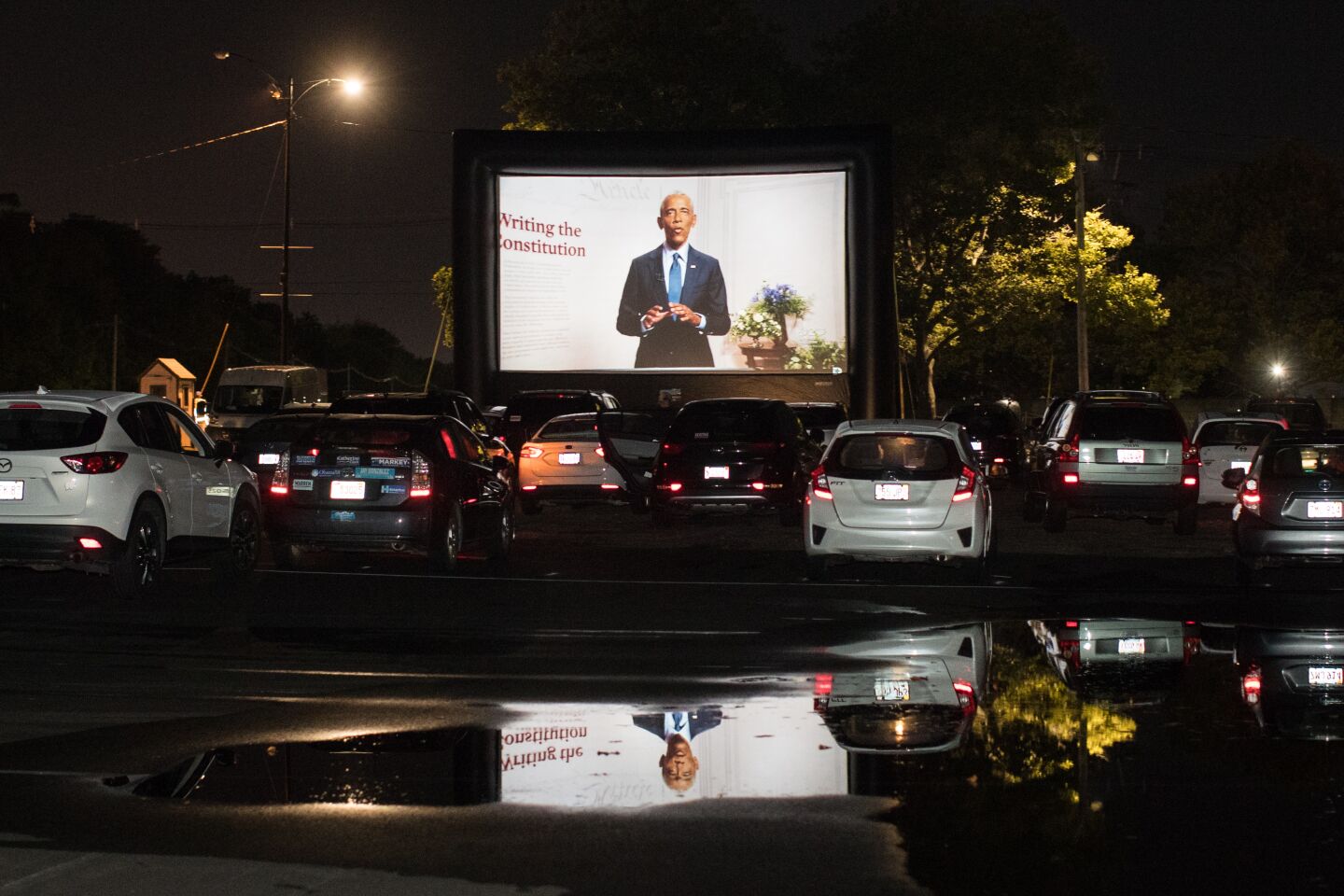 A screen projects former President Obama during a drive-in convention watch party in Boston.
