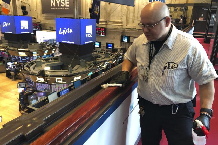 Porter Raul Rodriguez disinfects a railing at the New York Stock Exchange, Monday, March 9, 2020, amid coronavirus fears. (AP Photo/Ted Shaffrey)