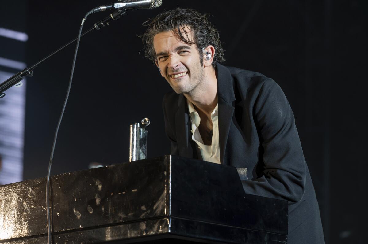 马蒂·希利 (Matty Healy) 穿着黑色夹克在音乐会上演奏键盘，脸上表情滑稽