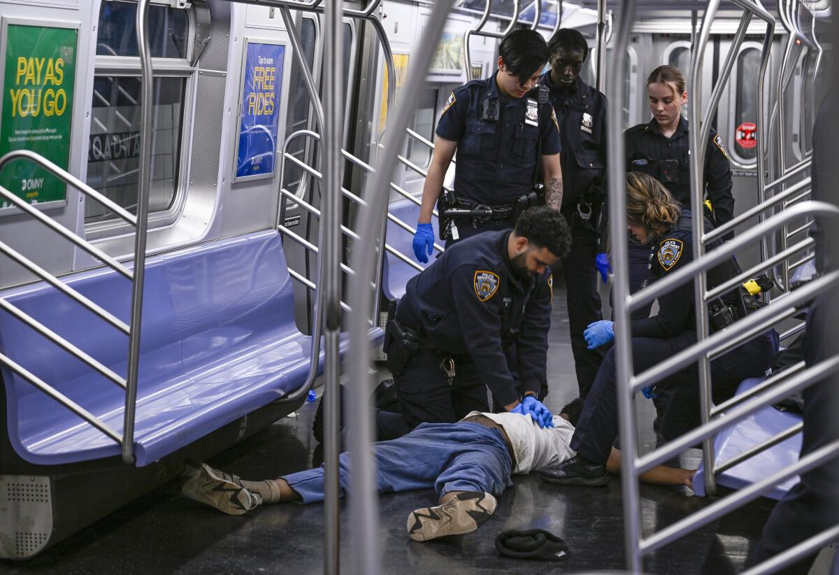 A police officer gives chest compressions to a man lying on the floor of a subway train as other officers stand around