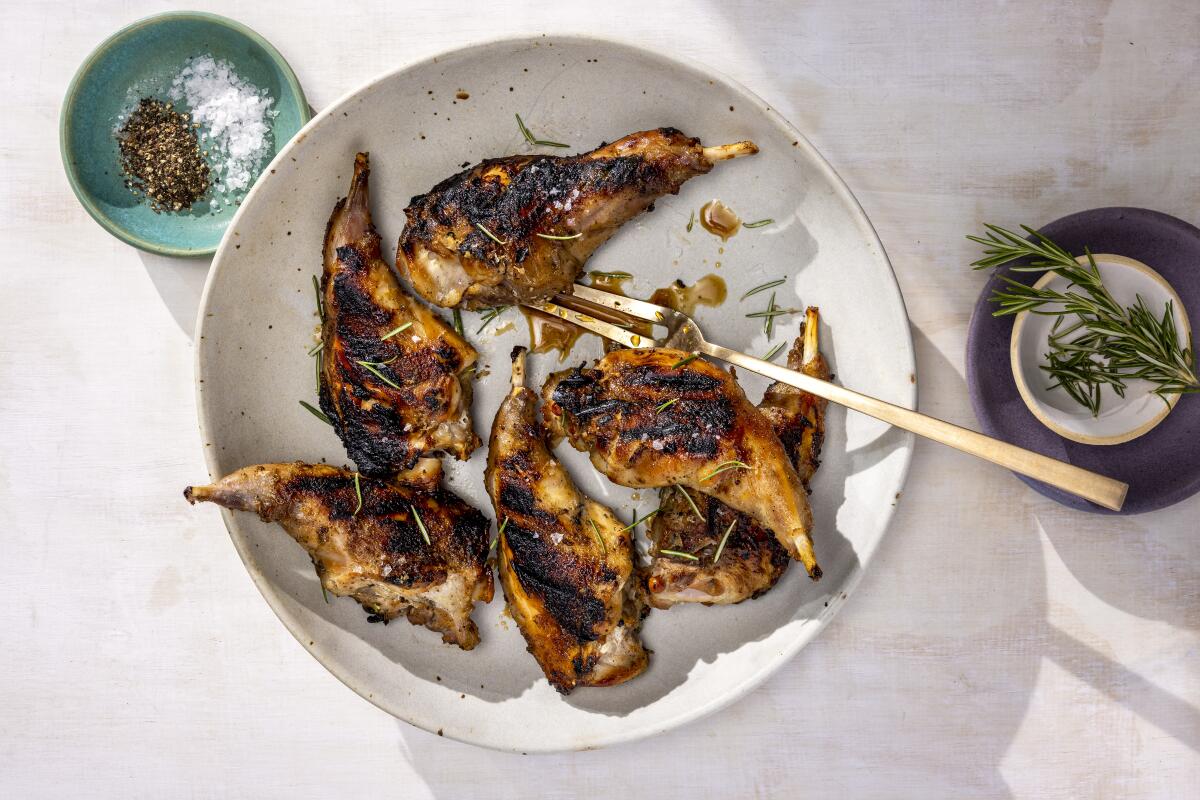 A white plate on a white tablecloth holds lightly charred pieces of rabbit.