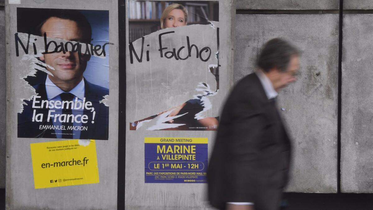A man walks by graffiti-marred election campaign posters in Rennes on Tuesday. The graffiti reads "Neither banker, nor fascist" over images of Emmanuel Macron and Marine le Pen.