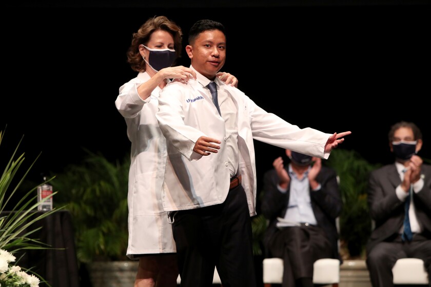 Ivann Agapito, right, is the first student to have his white coat put on by Jan D. Hirsch, at UCI's new pharmacy school.