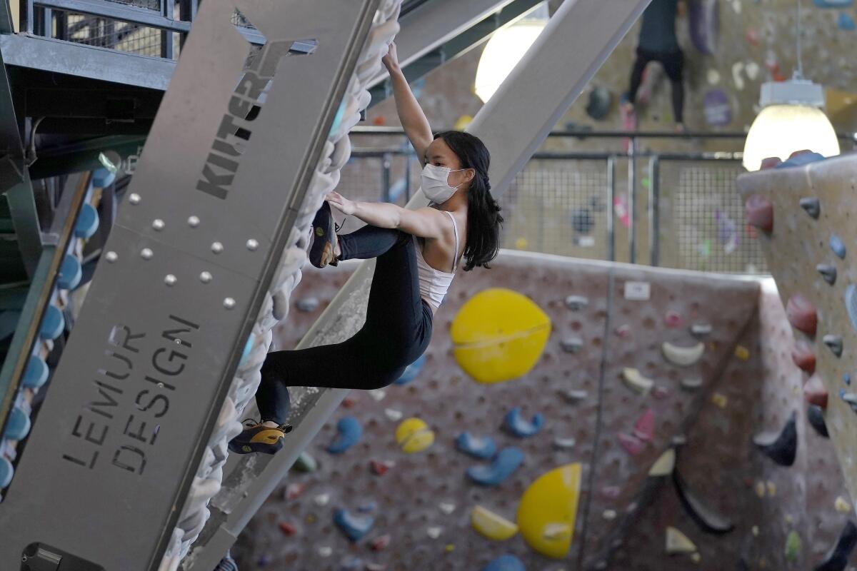 A woman wears a protective face mask while climbing a rock wall at a gym.