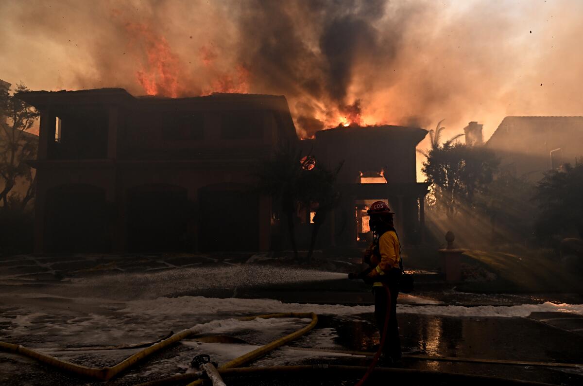 A firefighter sprays water in front of a burning home