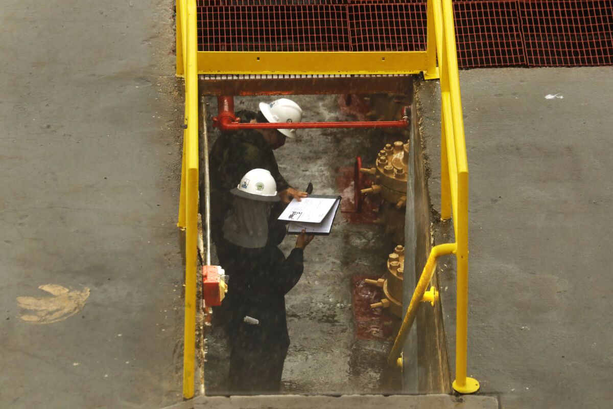 CalGEM inspectors in white hard hats at a oil drilling facility 