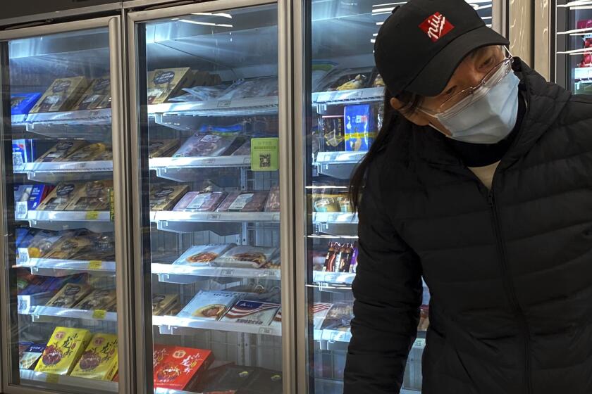 A woman wearing a face mask to help curb the spread of the coronavirus walks by a fridge displaying frozen meats at a supermarket in Beijing, Tuesday, Nov. 24, 2020. China has stirred controversy with claims it has detected the coronavirus on packages of imported frozen food. (AP Photo/Andy Wong)