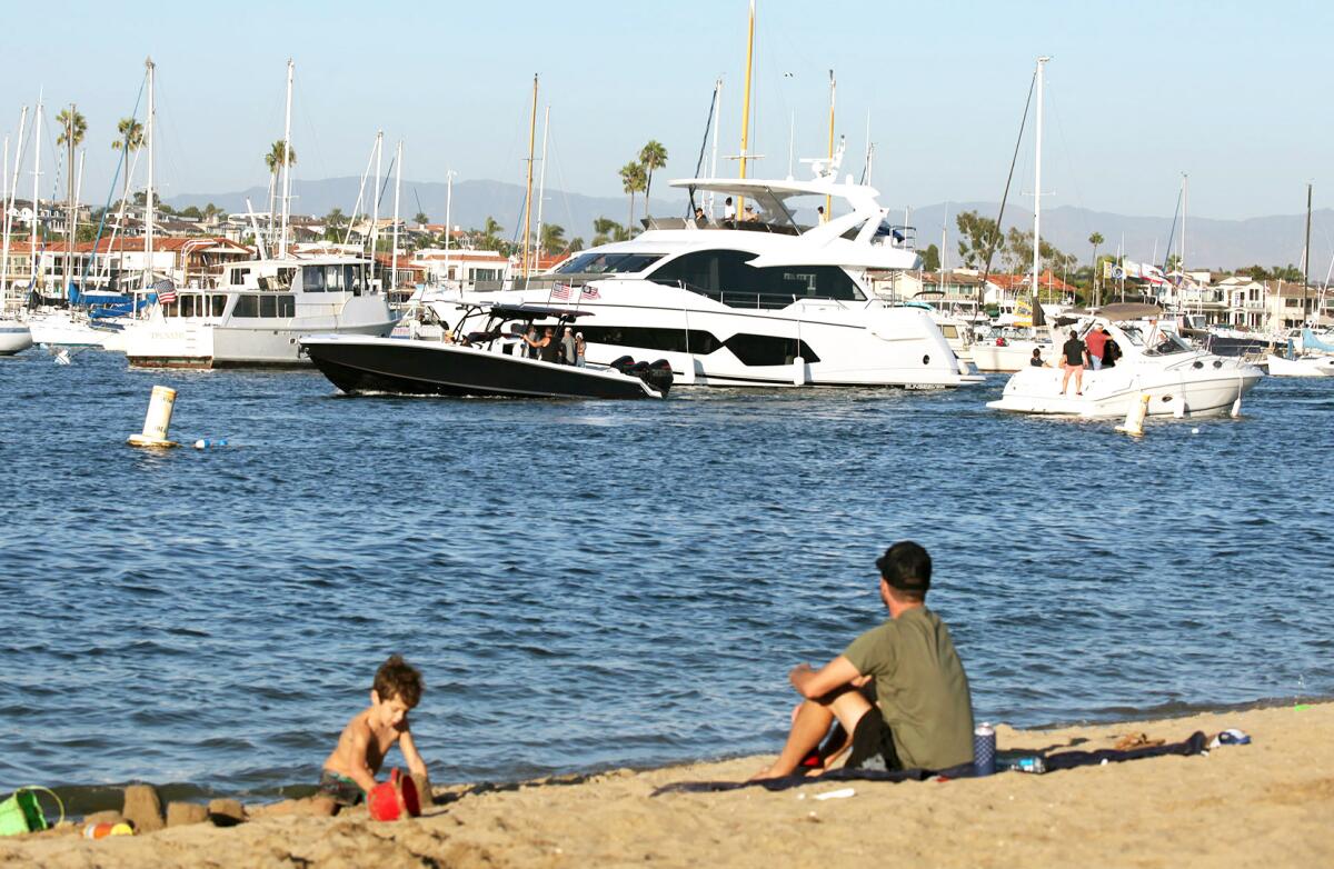 A father and son sit on the beach and watch boats take part in the 2021 War Heroes on Water (WHOW) Boat Parade. 