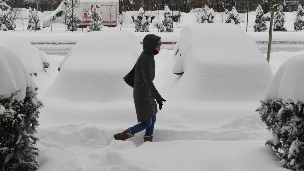 A woman walks next to snow-covered automobiles in Bucharest, Romania, on Jan. 11, 2016.