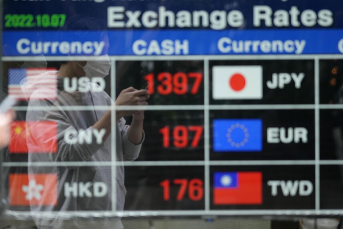 A man wearing a face mask is reflected on an electronic foreign currency exchange rates in downtown Seoul, South Korea, Friday, Oct. 7, 2022. Asian shares followed Wall Street lower Friday ahead of U.S. jobs data investors hope will persuade the Federal Reserve to ease off plans for more interest rate hikes. (AP Photo/Lee Jin-man)