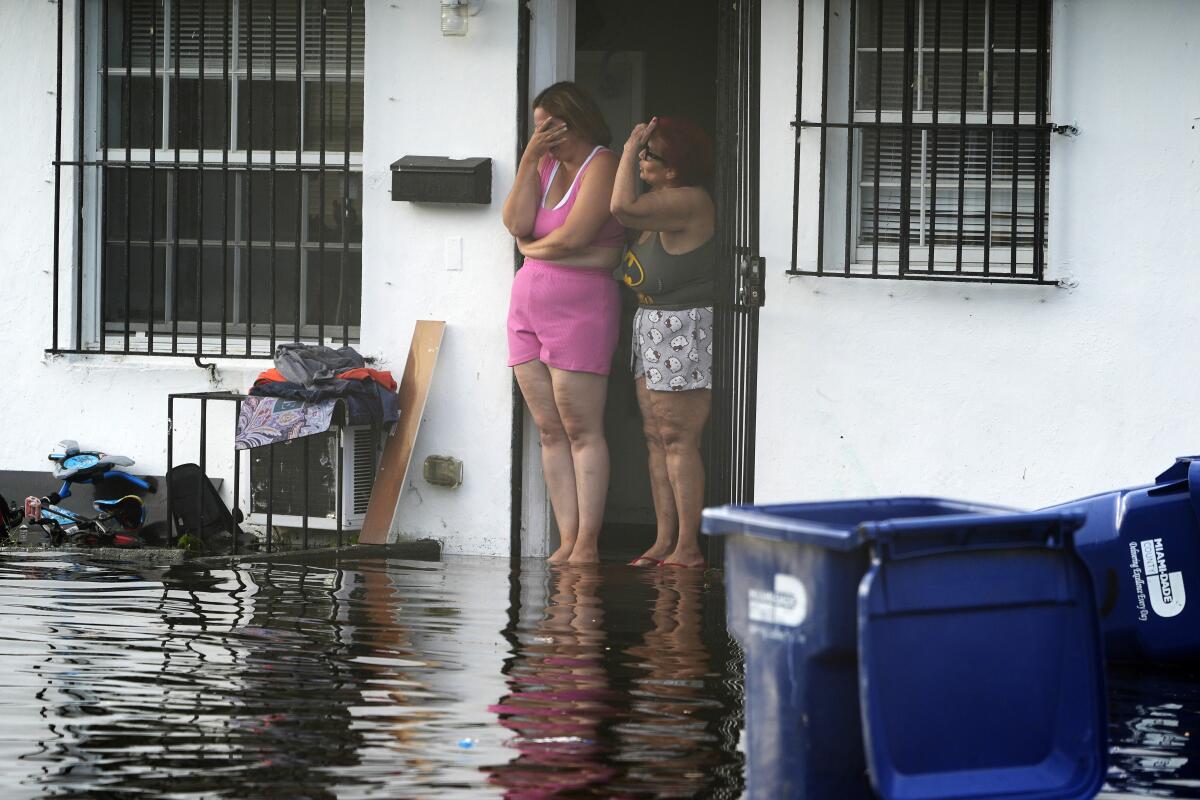 Two women react as they see flooding on their street in North Miami, Fla.