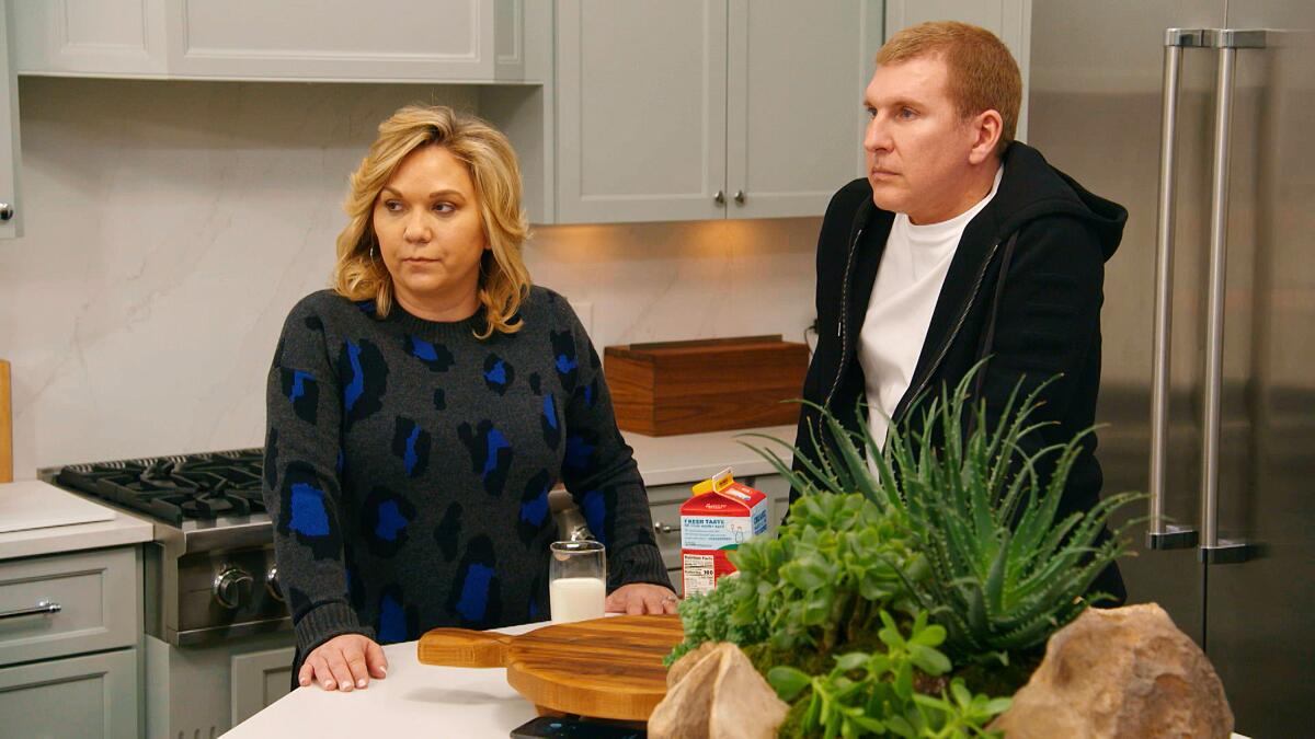 A woman and a man stand in a kitchen looking very serious