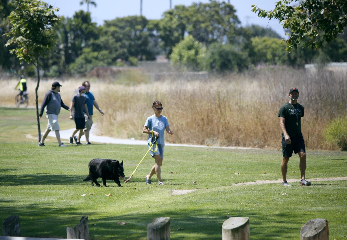 Steve and Mina Goeller, front, of Fountain Valley, walk their dog, Shadow, a black German shepherd, at Fairview Park in Costa Mesa on Saturday.