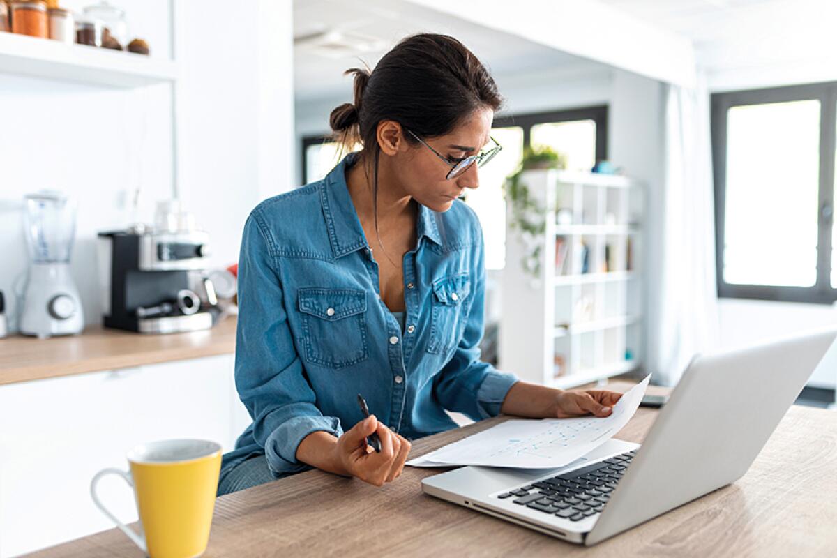 A woman reviewing paperwork and working on a laptop in a kitchen