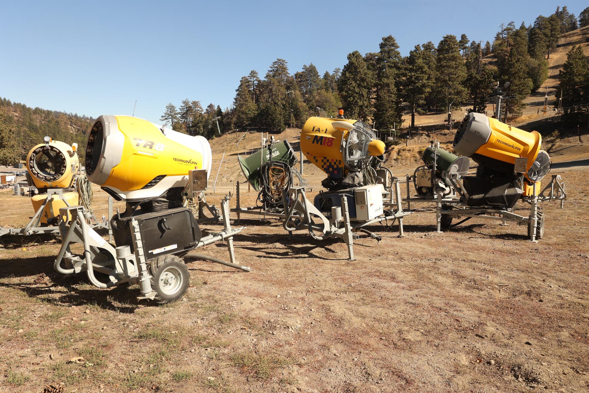 A handful of snowmaking machines stand on a hillside.