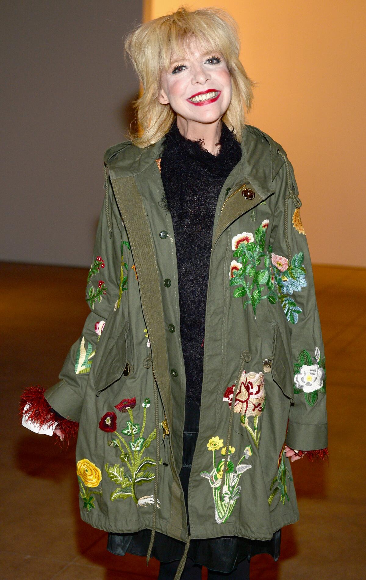  A blonde woman is a long army green jacket with flowers