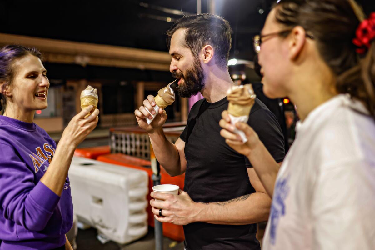 Three people stand in a store eating ice cream.
