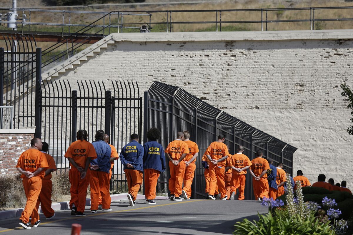 FILE - In this Aug. 16, 2016, file photo, general population inmates walk in a line at San Quentin State Prison in San Quentin, Calif. A Northern California judge tentatively ruled Friday, Oct. 15, 2021, that state prison officials acted with deliberate indifference when they caused a deadly coronavirus outbreak at the prison last year, but said vaccines have since so changed the landscape that officials are no longer violating inmates' constitutional rights. The lawsuit stemmed from the botched transfer of infected inmates in May 2020 from a Southern California prison to San Quentin. (AP Photo/Eric Risberg, File)