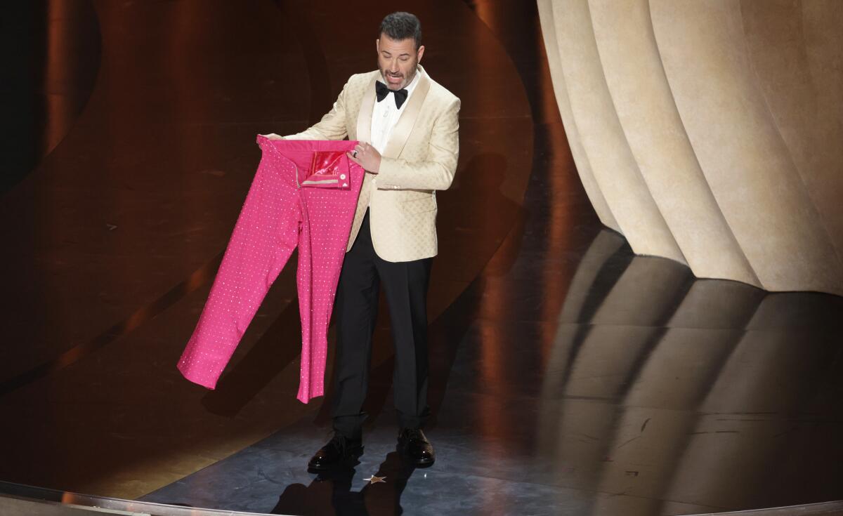 A host in a white jacket holds up a pair of pink pants.