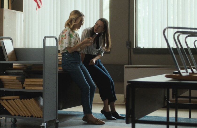 Two women lean on a desk