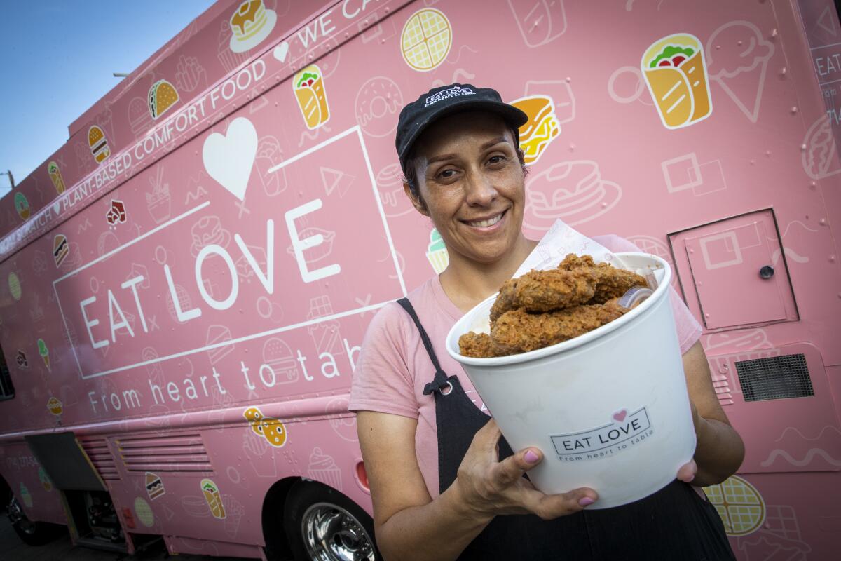 A woman holds the vegan fried chicken bucket from Eat Love in front of a pink food truck.