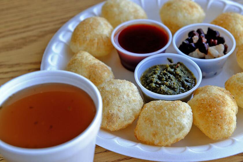 The pani puri, fluffed flour crisps, are served with spicy water, spicy sauce, sweet sauce, garbanzos and potatoes.