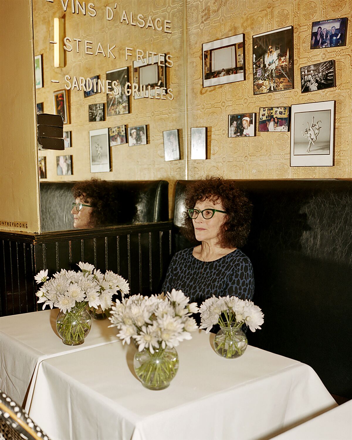 A woman sits in a restaurant banquette with vases of while flowers in front of her.
