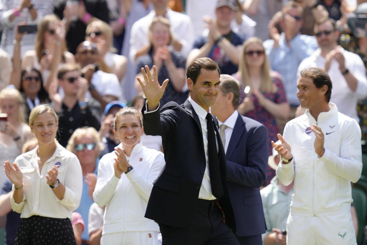 Roger Federer wears a suit and waves to fans at Wimbledon.