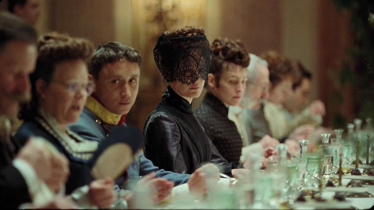 A masked woman and other people in Victorian evening dress sit at a table in the movie