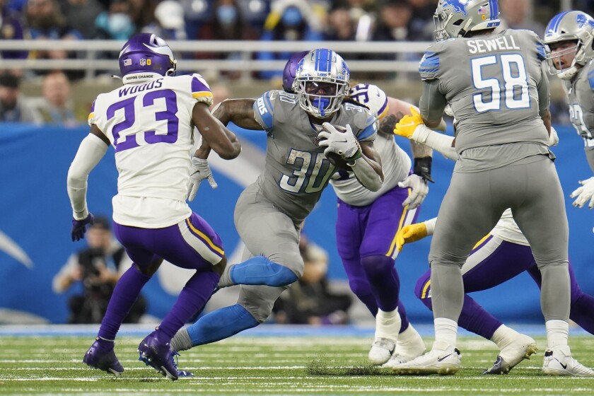 Detroit Lions running back Jamaal Williams (30) rushes by Minnesota Vikings free safety Xavier Woods (23) during the first half of an NFL football game, Sunday, Dec. 5, 2021, in Detroit. (AP Photo/Paul Sancya)