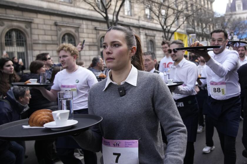 Meseros llevan bandejas con una taza de café, un croissant, y un vaso con agua mientras compiten en una carrera de camareros en las calles de París, el domingo 24 de marzo de 2024. (AP Foto/Christophe Ena)